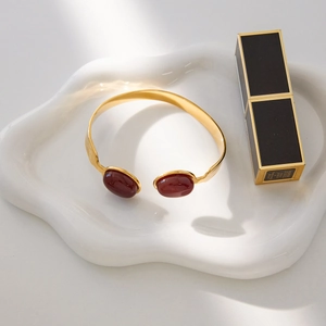 Macro shot of gold stainless steel bangle with red agate inlays on white tray