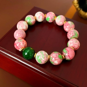 Close-up of gold-plated ceramic beaded bracelet with pink and green accents on a wood box