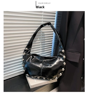 Detail of black glossy crescent bag with large silver metal studs on white background