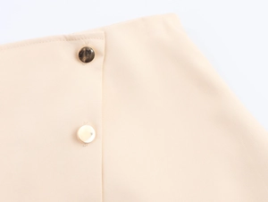 Detail of waist design on beige skort featuring asymmetric hem and gold metal buttons
