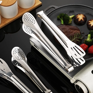 Polished stainless steel steak tongs set on a grill with cooked meat and vegetables
