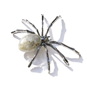 Detail of silver metal spider figurine with an oval white crystal stone on plain background