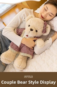Detail of a beige teddy bear in a red checkered lace dress on a cozy bed background