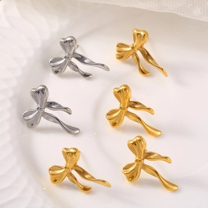Elegant gold and silver bow knot stud earrings on a minimalist white ceramic tray
