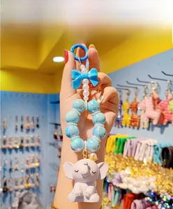 Detail of cute white elephant keychain with golden crown, blue beads, and bow ornament
