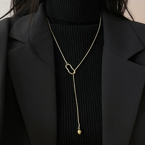 Detail of a minimalist gold chain necklace with a ring clasp and small gold ball pendant