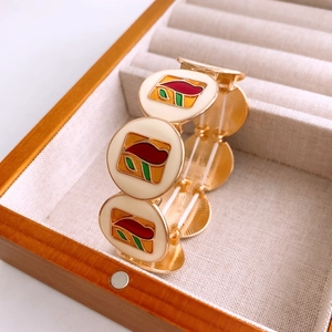 Close-up of vintage gold stretch bracelet with cream enamel floral patterns on wooden box