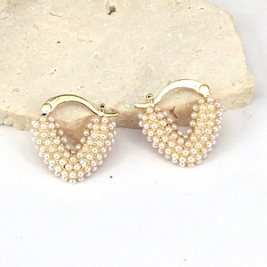 Detail of gold heart earrings with white seed pearls on a textured stone surface