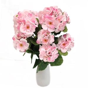 Detailed close-up of realistic pink silk geranium flowers with green leaves in a white vase