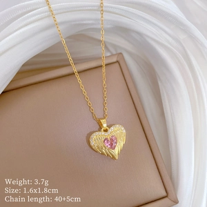 Detail shot of a gold necklace featuring a pink heart stone and angel wing pendant