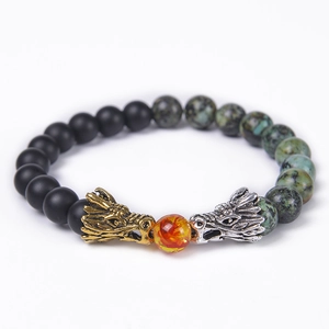 Macro shot of gold and silver dragon head charms with matte black and tiger eye stone beads