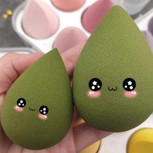 Two green teardrop makeup sponges with cute cartoon faces for wet and dry dual use