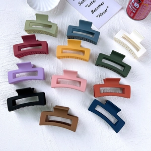 Flat lay of 12 colorful matte square shark hair clips on textured white fabric background