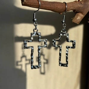 Detailed view of silver cross earrings with hammered texture hanging on a wooden branch