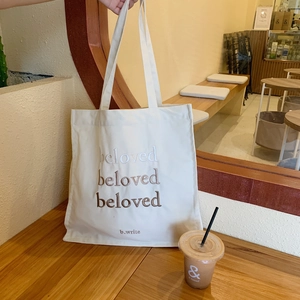 Close-up of the beloved embroidered lettering on the cream-colored canvas tote bag