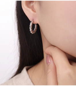 Macro shot of silver C-shape earrings with textured spiral design on model's ear