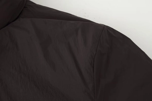 Detailed view of deep brown nylon jacket shoulder featuring smooth fabric and fine stitching