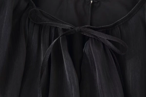 Dettaglio dell'abito corto nero con scollo a fiocco e raffinata trama plissettata