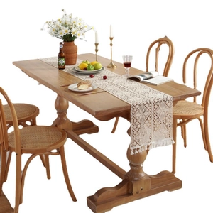Beige lace table runner with crochet floral patterns and tassels on a wooden dining table