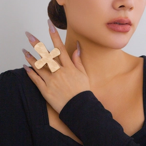 Detailed close-up of a large gold cross ring with intricate spiral texture on model