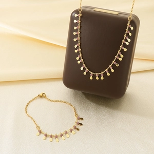 Detail of gold necklace and bracelet set with purple beads on beige silk background