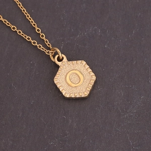 Macro shot of gold hexagon necklace pendant with letter O and grainy metal texture