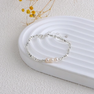 Detail of silver beaded necklace with three white pearls on a minimalist white tray