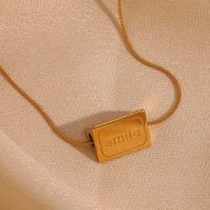 Nahaufnahme des 18K vergoldeten Smile-Anhängers an einer Schlangenkette auf Seide