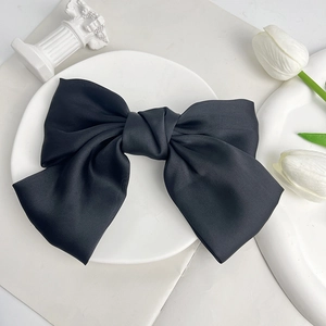 Detail of a large black satin bow hair clip on a minimalist white display background