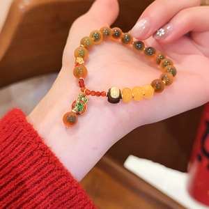 Detailansicht eines roten Achat-Perlenarmbands mit einem goldenen Kürbis-Anhänger am Arm