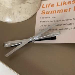 Detailed view of silver ribbon bow hair clip on a metal tray for a chic minimalist aesthetic