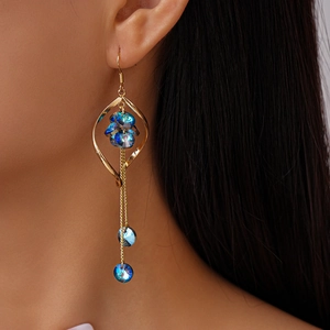 Macro side view of a gold tassel earring with blue crystals worn on a model's ear