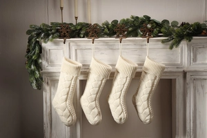 Set of four white knitted Christmas stockings with intricate woven patterns on a mantel