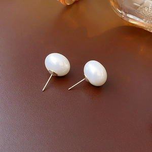 Detailed view of glossy white pearl earrings with elegant gold posts on brown texture
