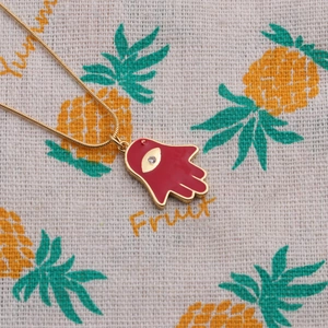 Detailed view of a gold-plated Hamsa hand necklace with red enamel and a central zircon stone