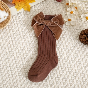 Close-up of brown velvet bow on knit baby socks with autumn pine cones and maple leaves