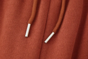 Makroaufnahme von rostrotem Strickstoff mit Kordelzug und silbernen Metallspitzen