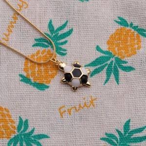 Detail of a gold turtle necklace with patterned shell on a decorative pineapple fabric background