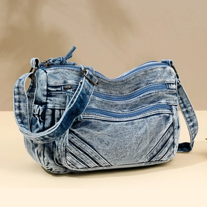Light blue washed denim crossbody bag with multiple zipper layers and adjustable strap
