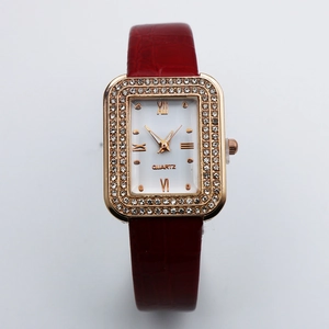 Detail of rose gold rectangular watch with crystal bezel and red leather strap