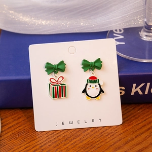 Detail of Christmas earrings featuring a festive penguin, gift box, and green ribbon bow