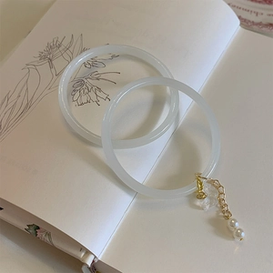 Close-up of a creamy white jade-textured bangle with pearl and flower charms on a book