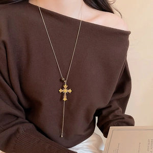 Golden cross necklace with yellow gemstone on model wearing a brown knit sweater