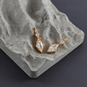 Detail of 18k gold plated earring with marquise cut zircon on grey textured stone