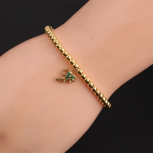Détail du bracelet à perles dorées avec pendentif palmier et cristaux verts