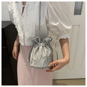 Silver glossy drawstring bucket bag with pleated texture worn on model's shoulder