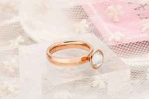 Dettaglio anello in oro rosa con zircone tondo trasparente su sfondo in pizzo bianco
