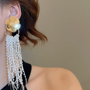 Detail of floral gold earrings with long white beaded tassels worn by a model