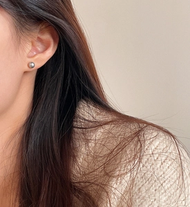 Macro shot of minimalist silver grey round pearl stud earrings on a female ear
