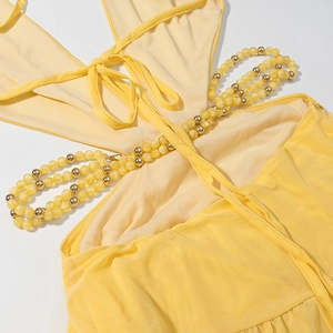 Detail of backless yellow dress featuring intricate beaded chains and lace-up design